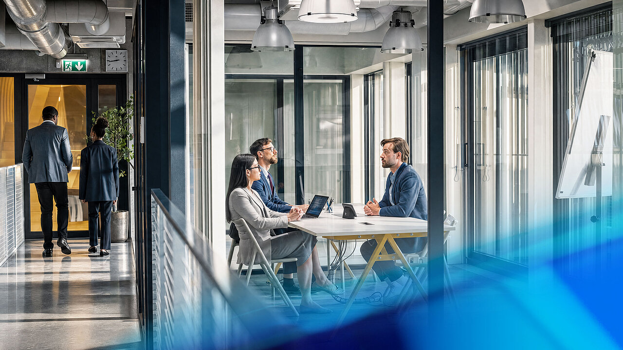Drei Personen diskutieren Projekte und strategische Themen an einem Besprechungstisch in einem modernen Büro.