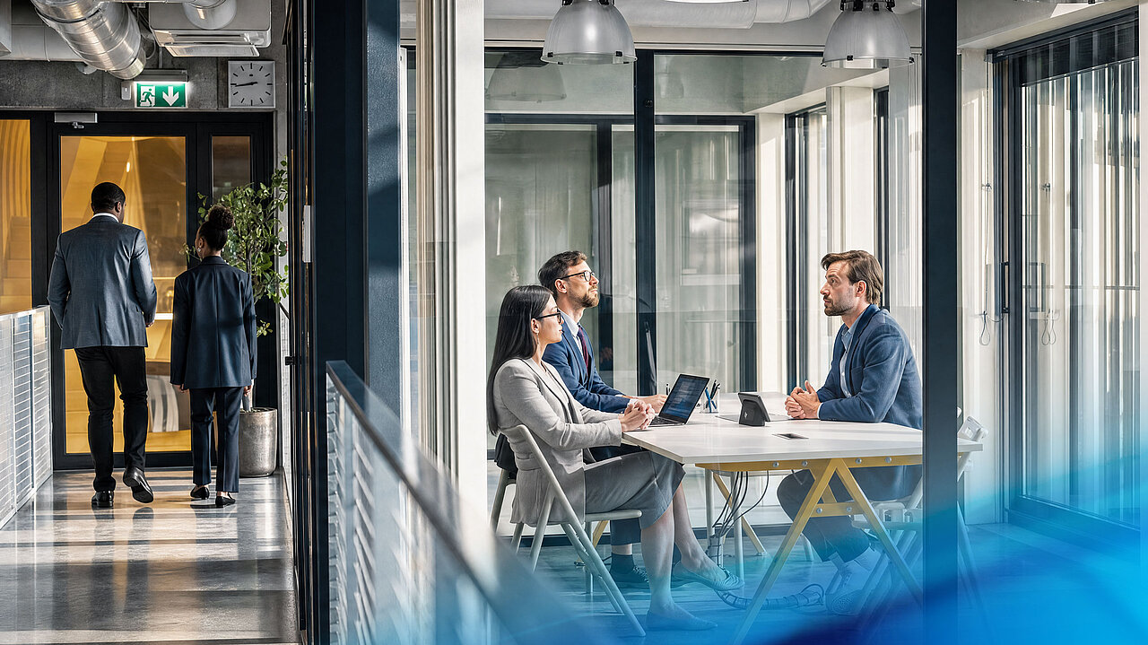 Drei Personen diskutieren Projekte und strategische Themen an einem Besprechungstisch in einem modernen Büro.