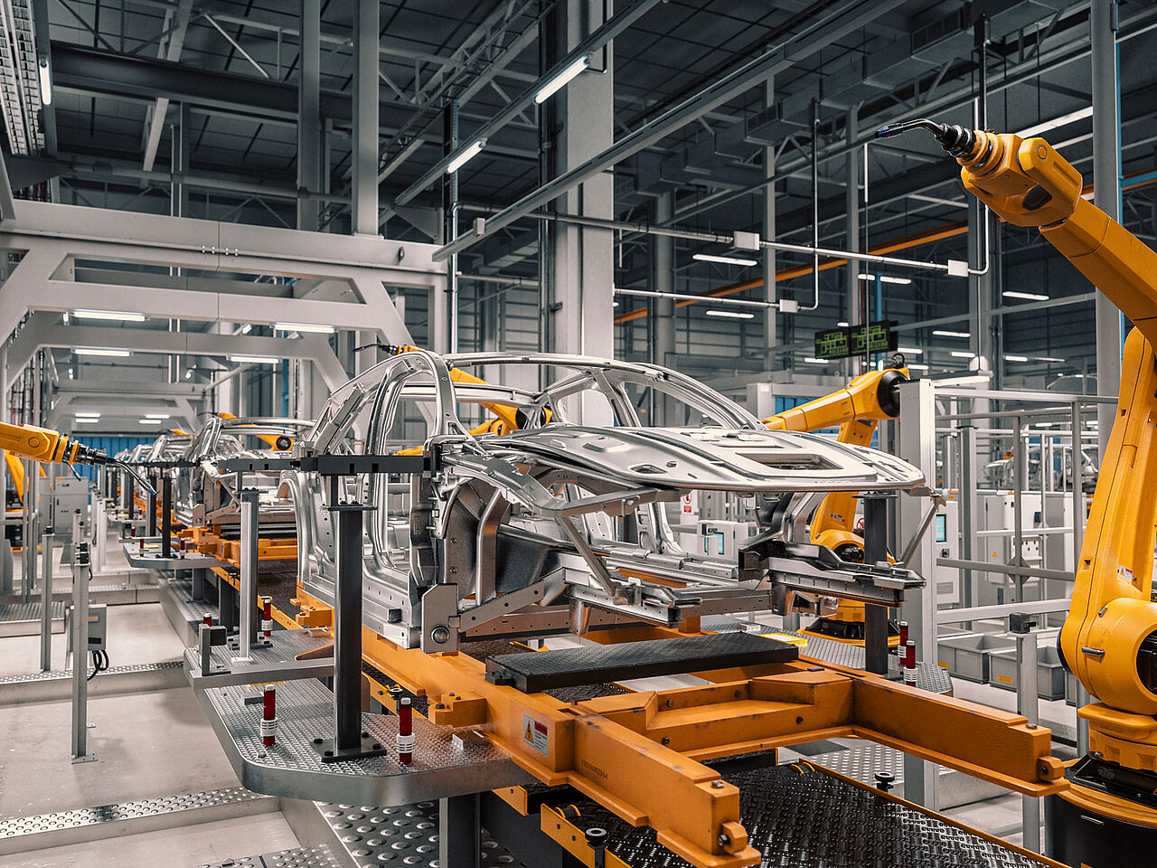 Automatisierte Fertigungslinie in der Automobilproduktion mit gelben Industrierobotern, die eine Fahrzeugkarosserie bearbeiten.